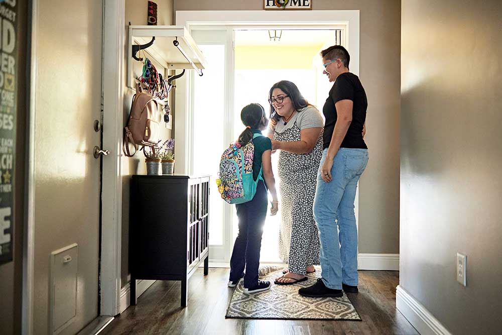 Parents get daughter ready to leave for school at home doorway