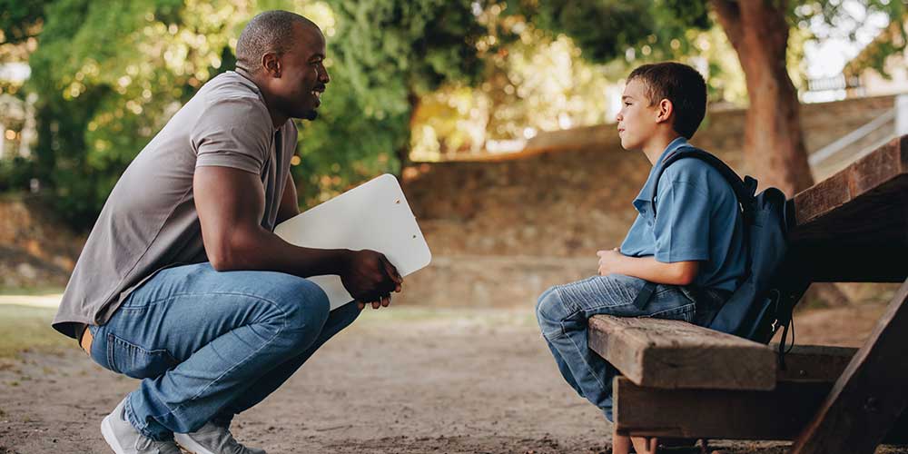 adult speaking with young man while sitting on a bench